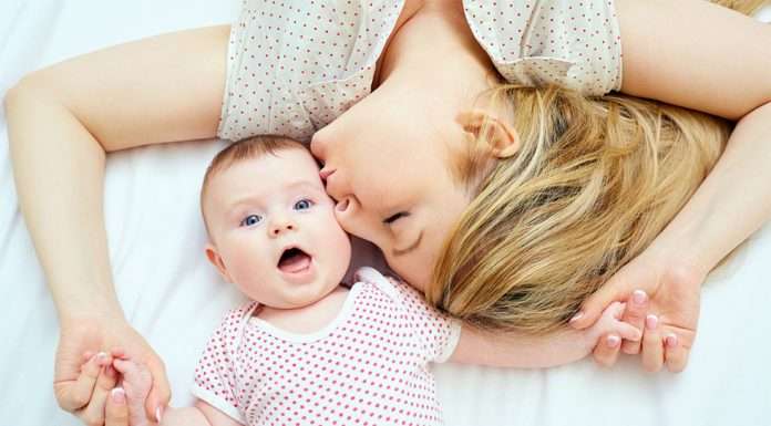 nainen makaa sängyllä vauvan vieressä ja antaa pusun