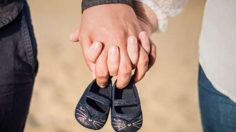 Valokuva pariskunnan käsistä ja pienet kengät – selkeä ja suloinen viesti siitä, että odotatte vauvaa! Kuva: iStock