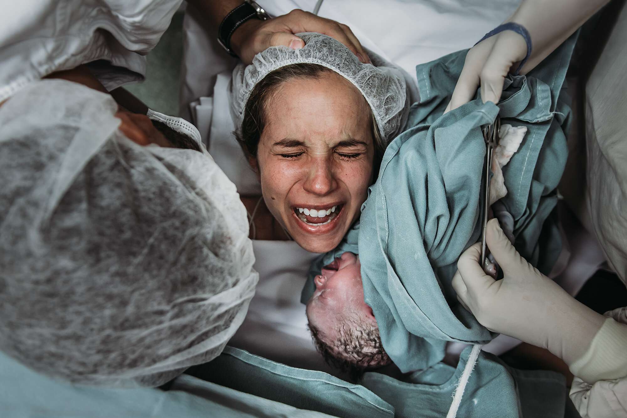 Tunnetta täynnä oleva välähdys keisarileikkauksesta, kun vastasyntynyt lapsi nostetaan ensi kertaa äidin kasvojen lähelle. Kuva: Deborah Elenter, kaikki artikkelin kuvat käytössä Birth Becomes Her -verkkosivuston luvalla.