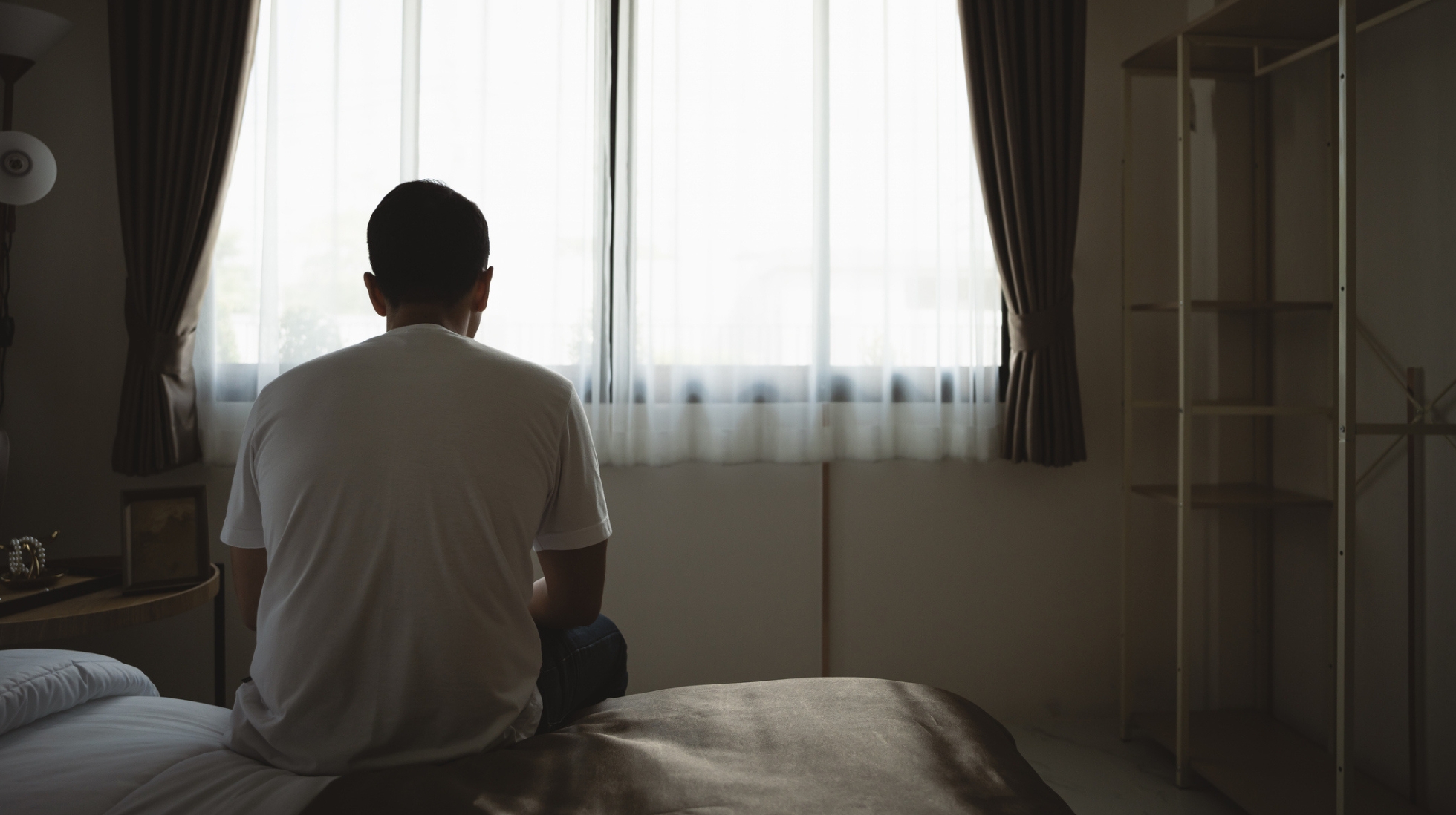 Mies istuu sängyllä hämärässä huoneessa