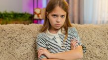 Miksi lapsi kiusaa? ”Rankaiseminen harvoin auttaa mitään” Vihainen tyttölapsi istuu sohvalla ja tuijottaa kameraan