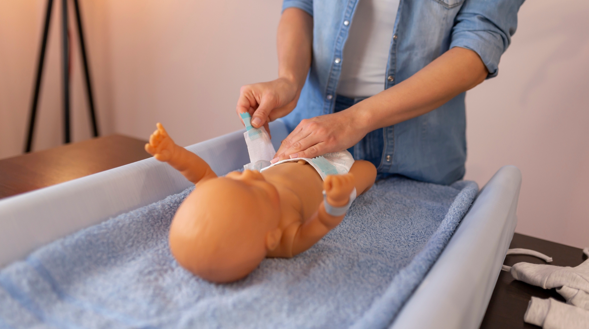 Henkilö harjoittelee hoitopöydällä vaipan vaihtoa nukelle
