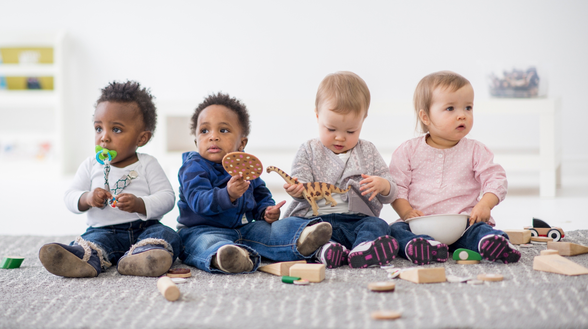 Neljä taaperoa istuu lattialla ja leikkii