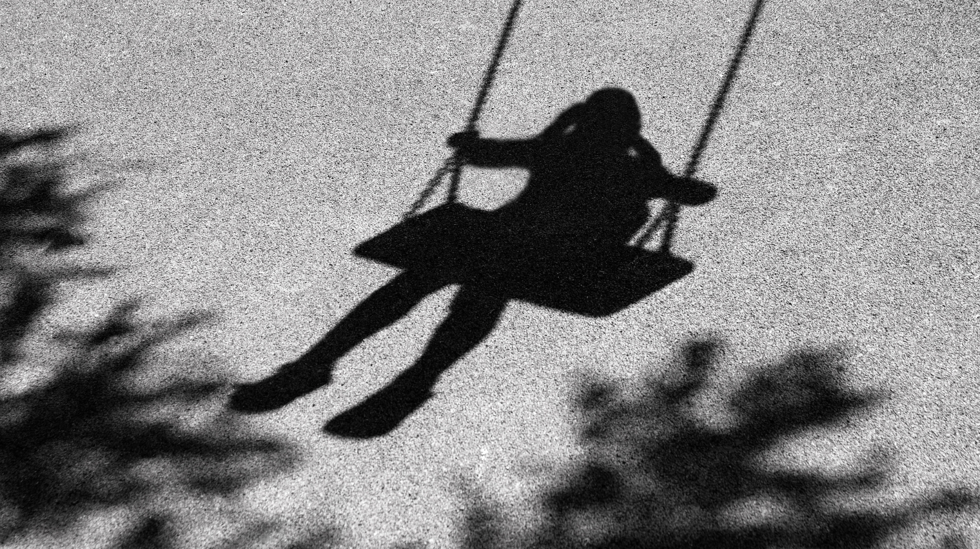 Varjosiluetti puiden katveessa keinuvasta lapsesta.